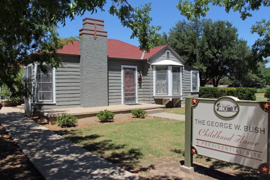 Exterior of the George W. Bush Childhood Home in Midland, Texas, with a historical marker sign and a well-kept lawn under shaded trees.